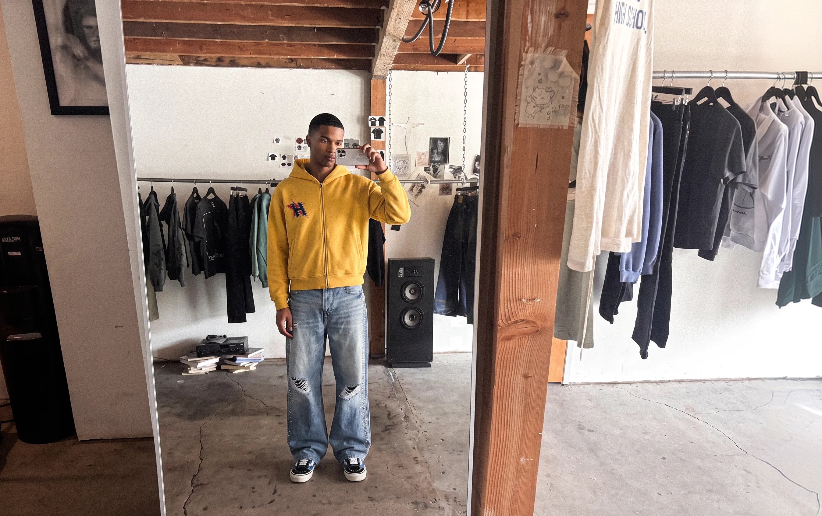 Model in a yellow hoodie taking a mirror selfie in a clothing studio