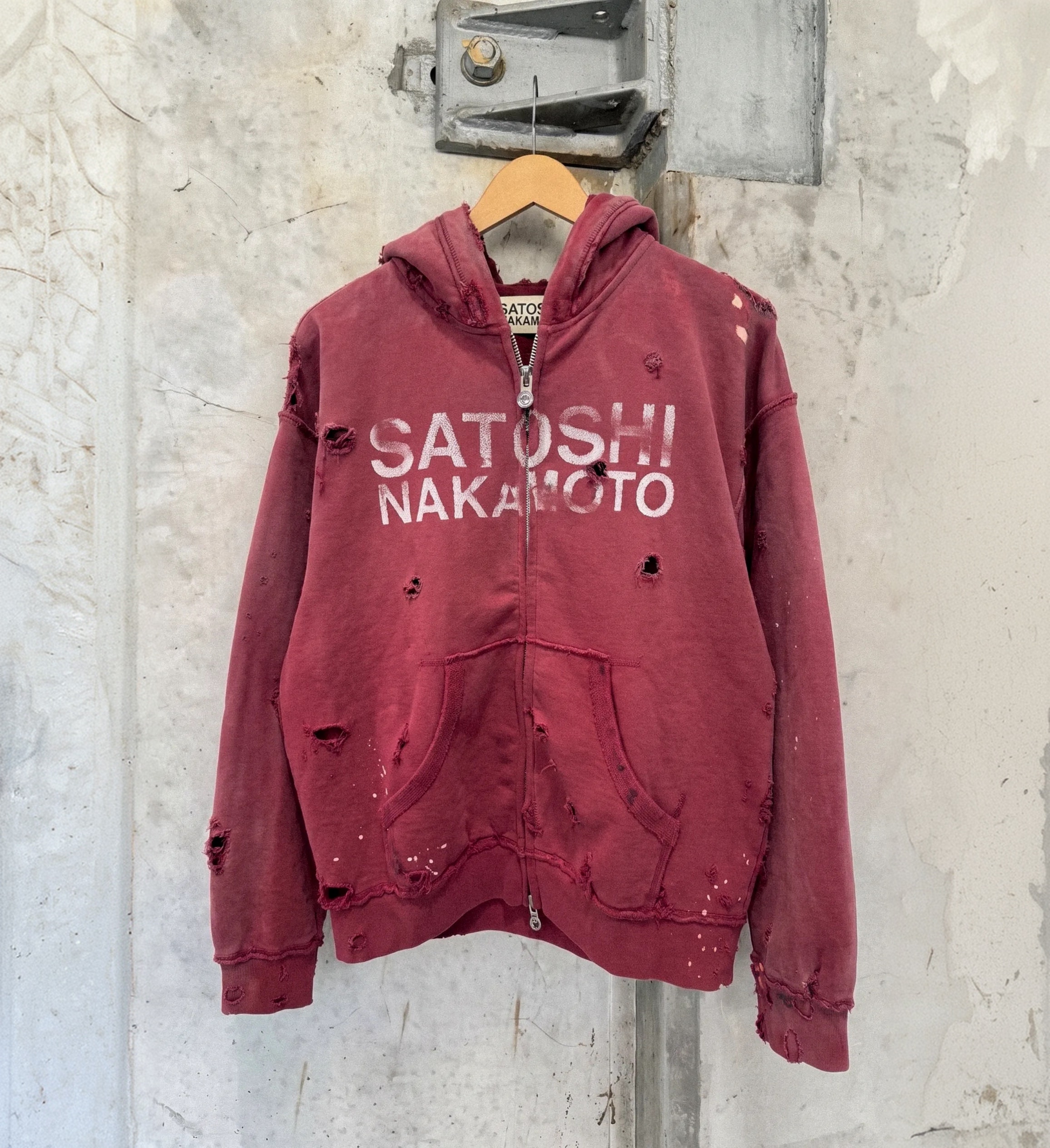 Distressed red zip hoodie on a hanger against a concrete wall