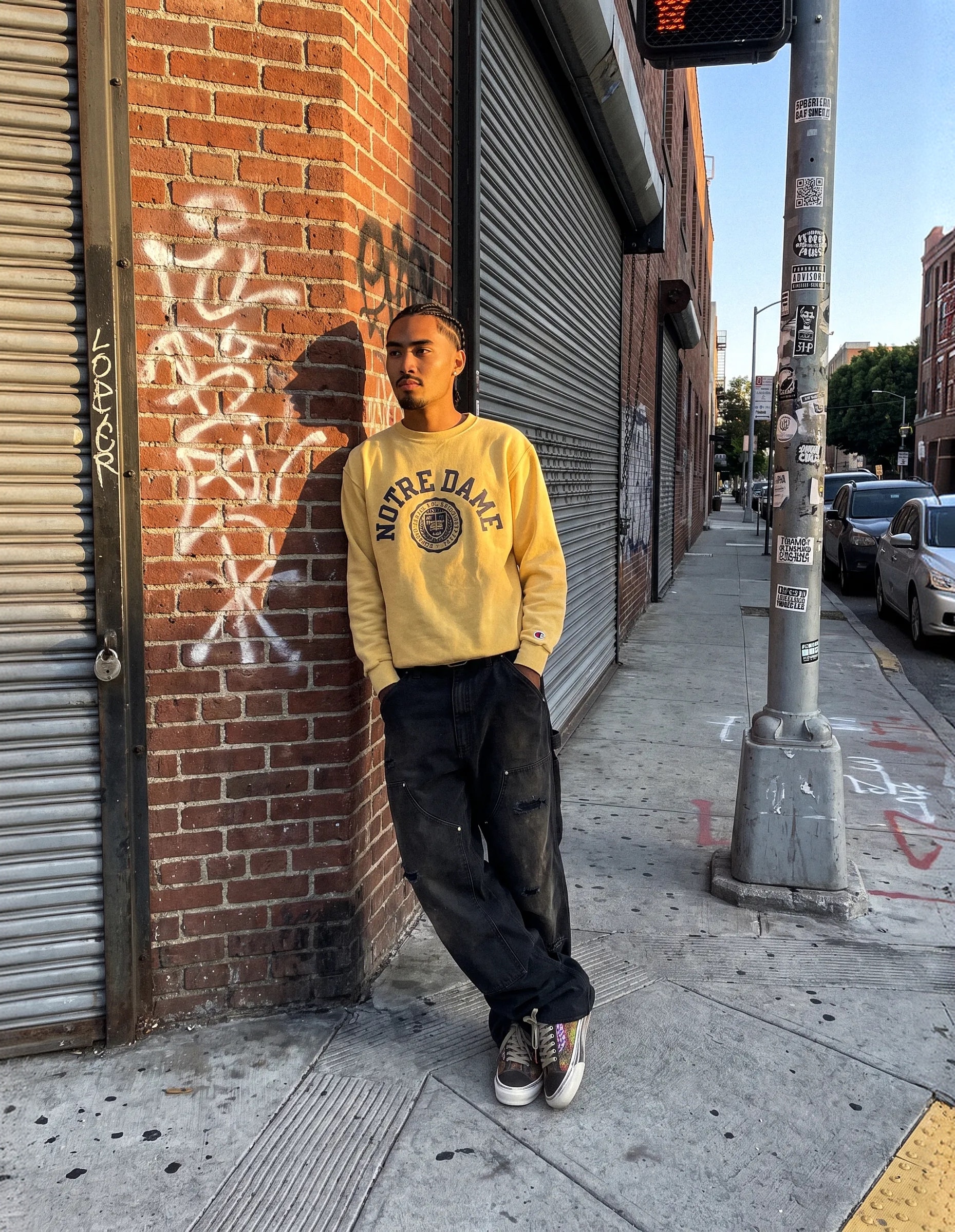 Model in a yellow crewneck leaning on a graffitied brick wall